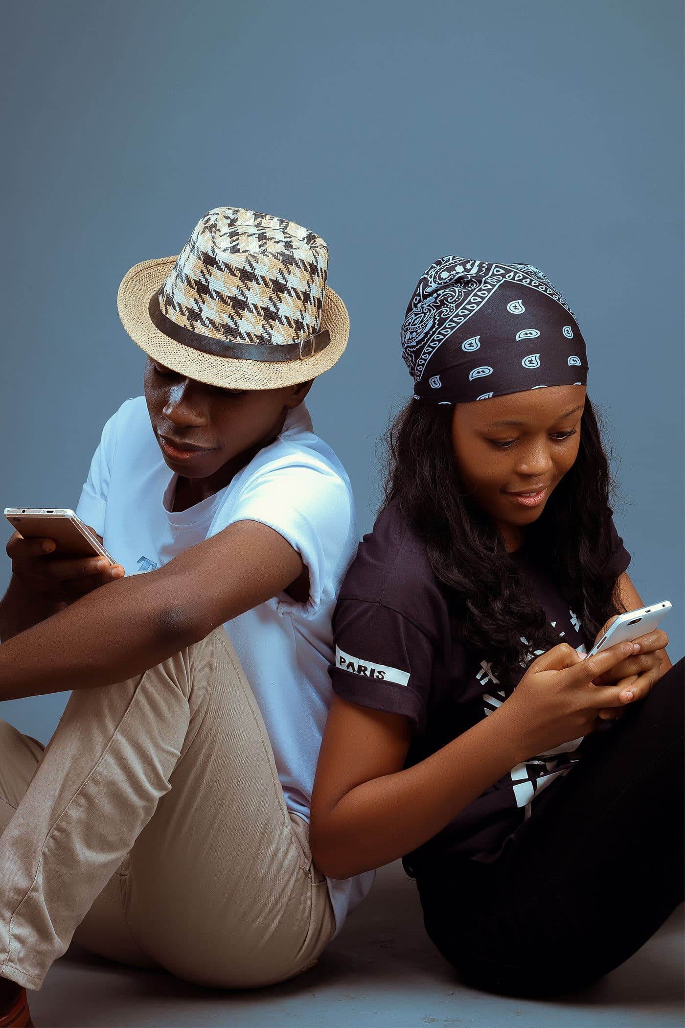 Deux jeunes assis dos à dos, chacun concentré sur son téléphone.